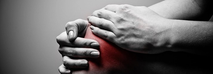 Person holding a painful knee in a black-and-white clinical image